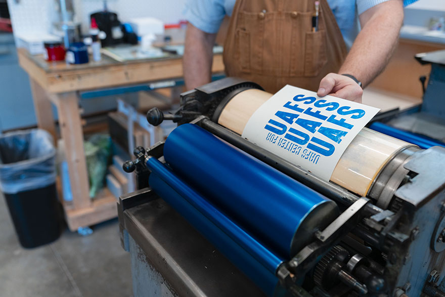 Jay Fox guiding a letterpressed material through the letterpress machine