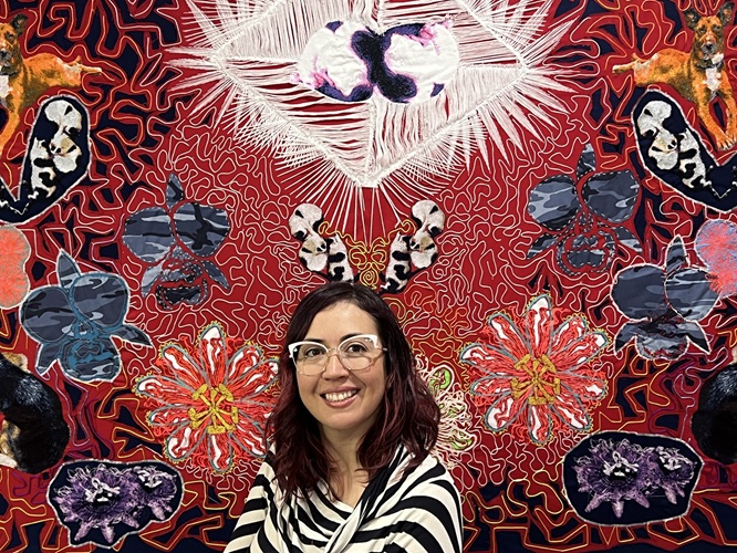 Artist Johana Moscoso sits in front of a colorful mural