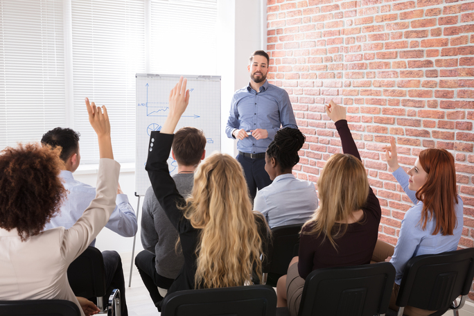 Adult Learners with their hands raised in a classroom setting