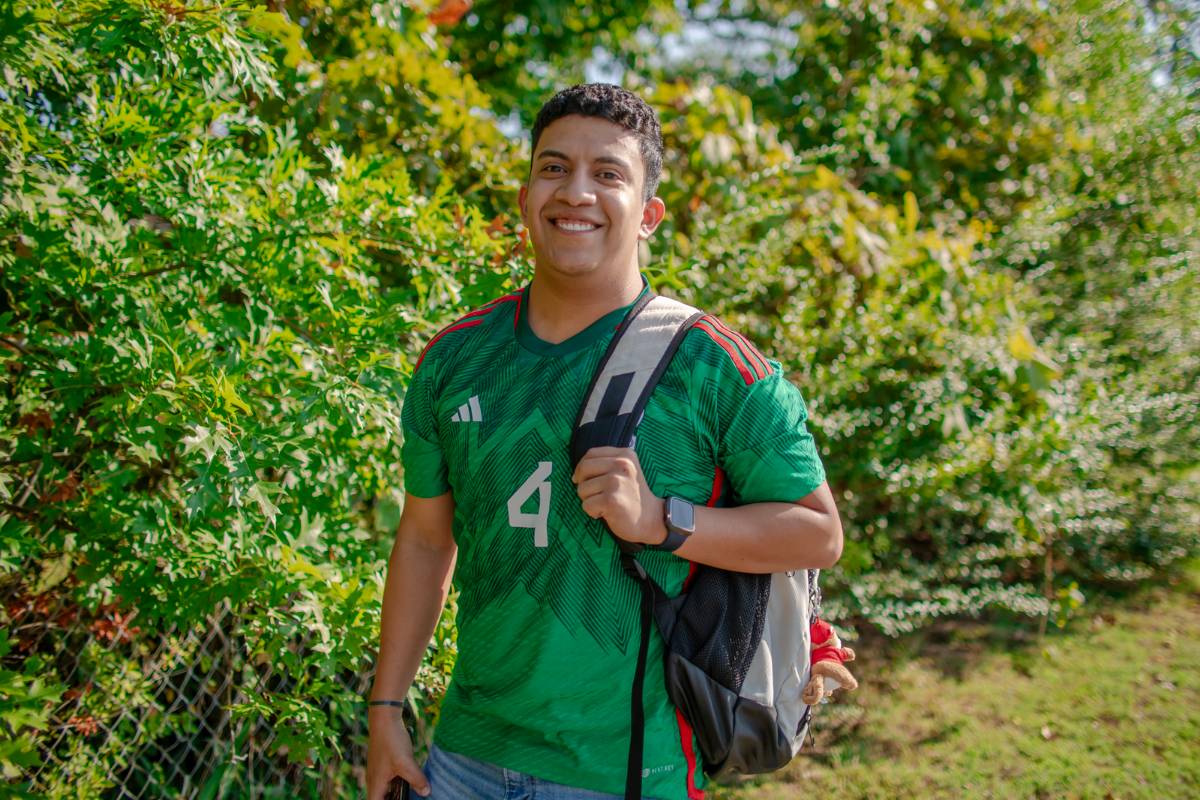Jesus smiling while standing next to a bush with his backpack on.