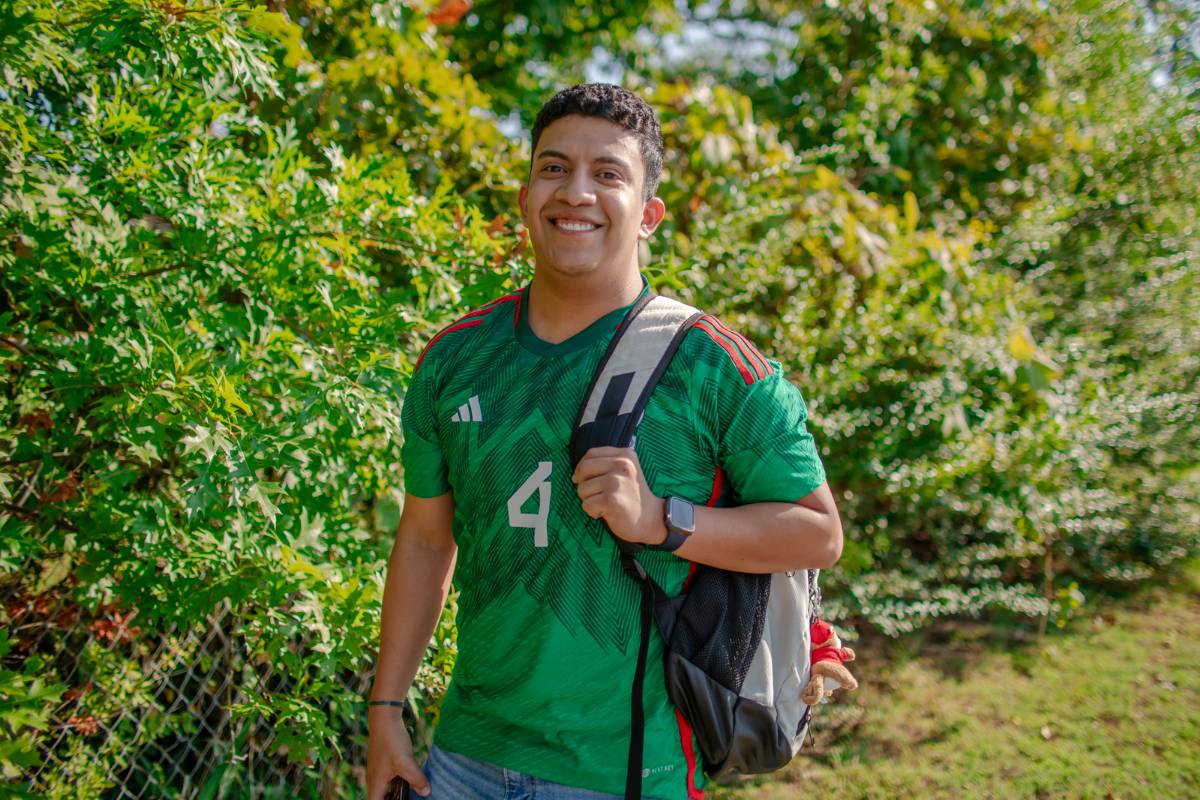 Jesus smiling while standing next to a bush with his backpack on.