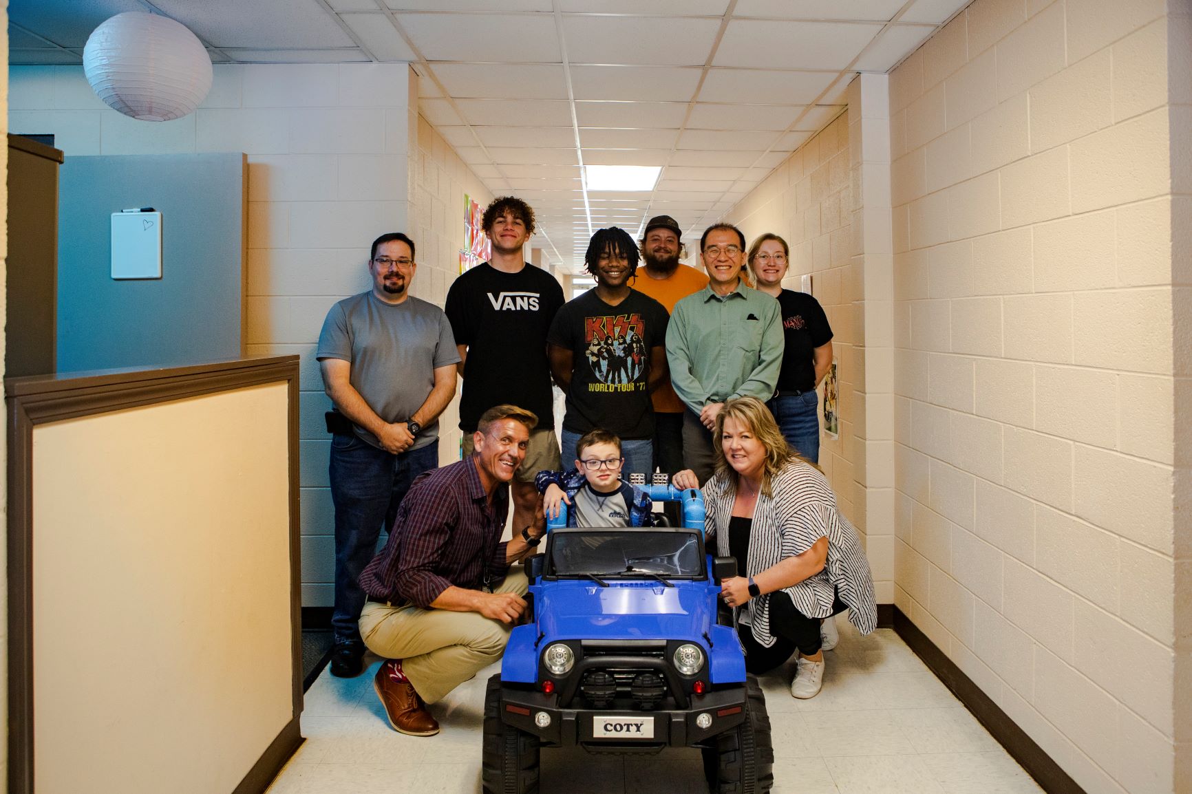 Adults surround a young child in a child's riding car