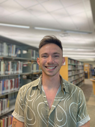 Smiling person standing in front of library shelves filed with books