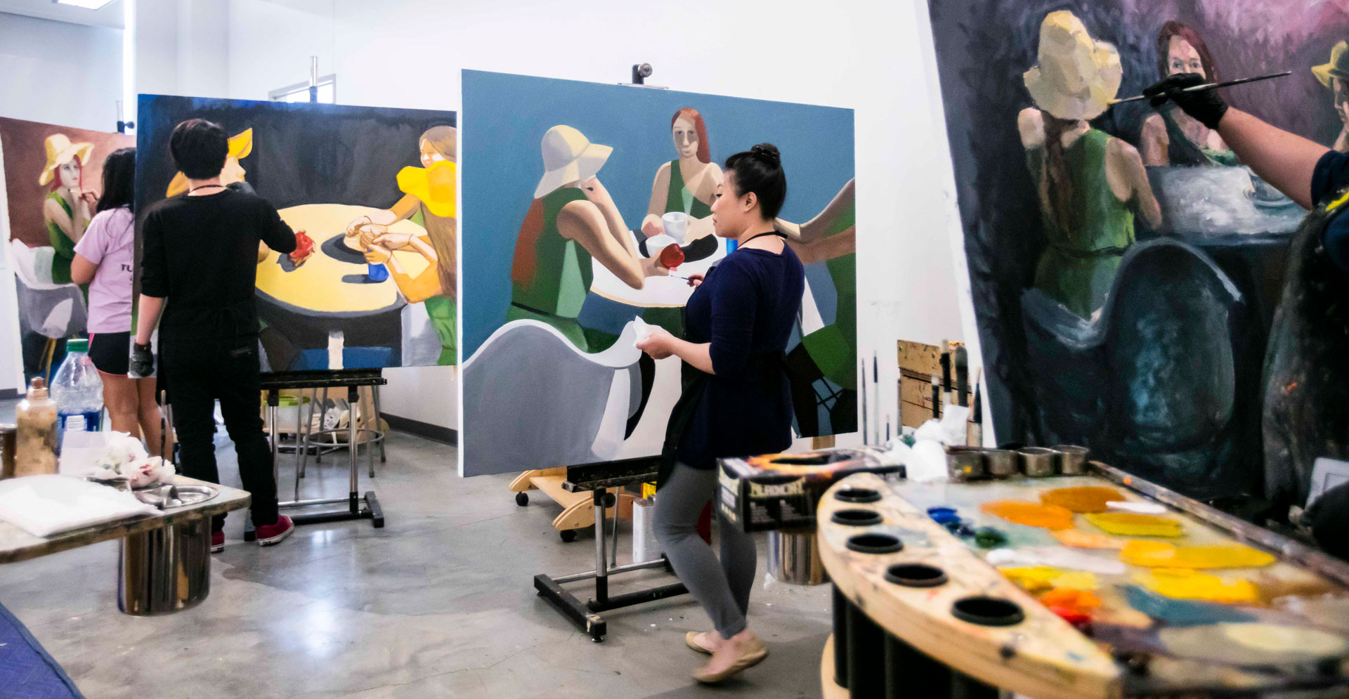 Three people paint individual colorful paintings in a classroom.