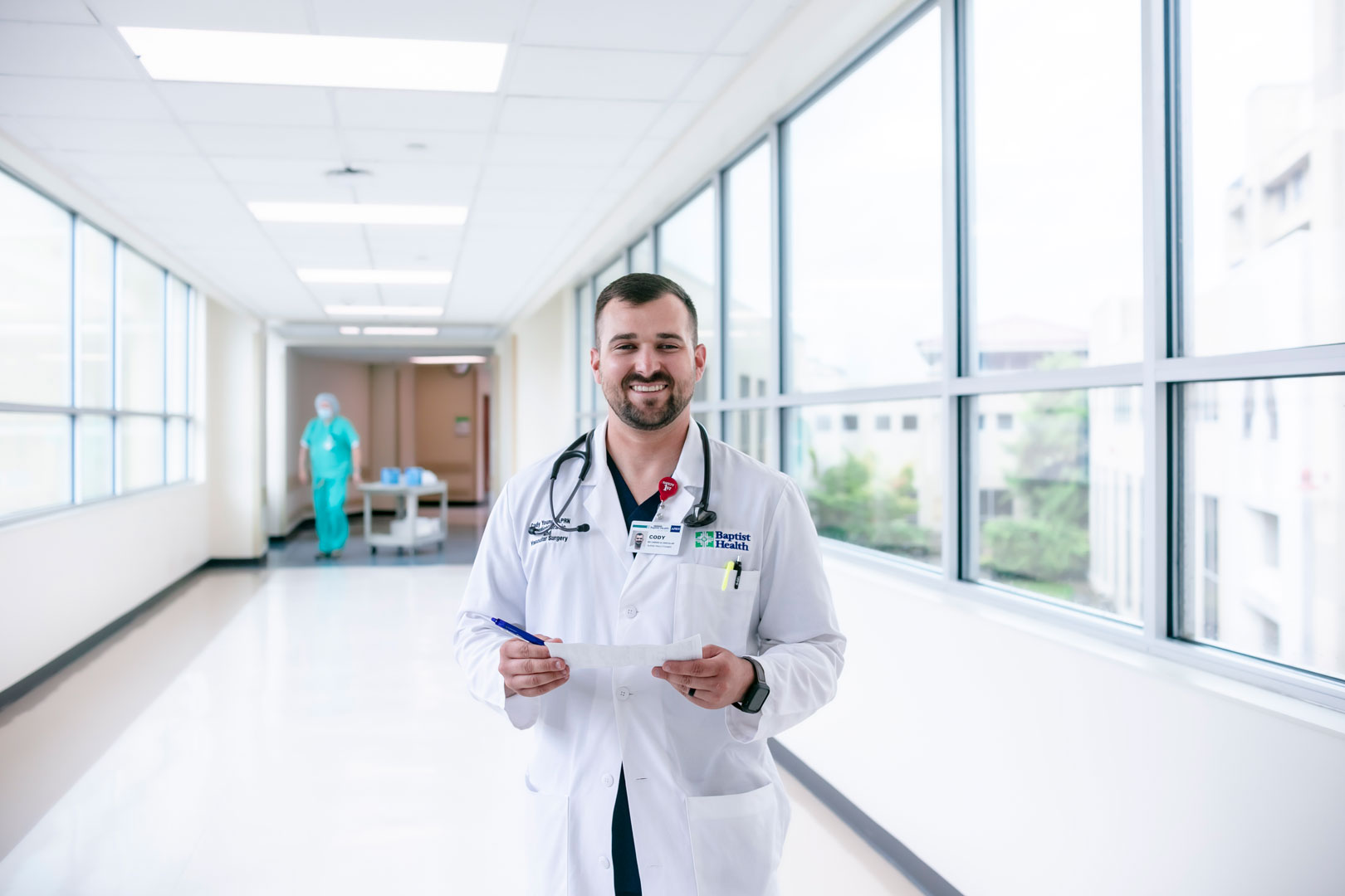 A nurse practioner in a white medical coat poses for photo in medical setting.