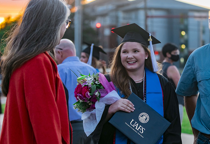 UAFS graduate in cap and gown smiling