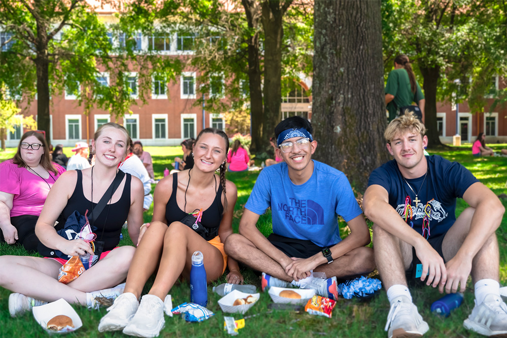 A group of students sit in the shade while eating lunch on the UAFS Campus Green.