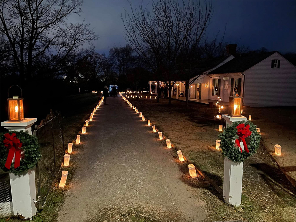 The Drennen-Scott Historic Site sits in the background with the walkway leading up to the house lined with candles and holiday wreaths.