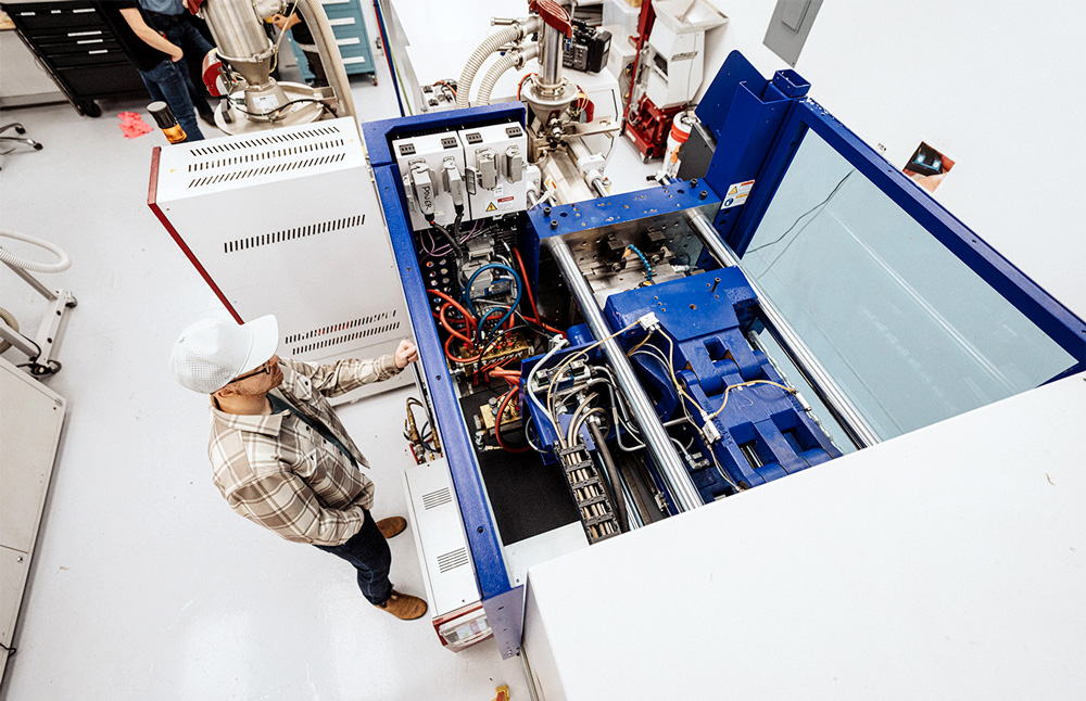 High angle view looking down at a male worker operating a a plastic injection molding machine in a clean room located in a manufacturing and fabrication facility.