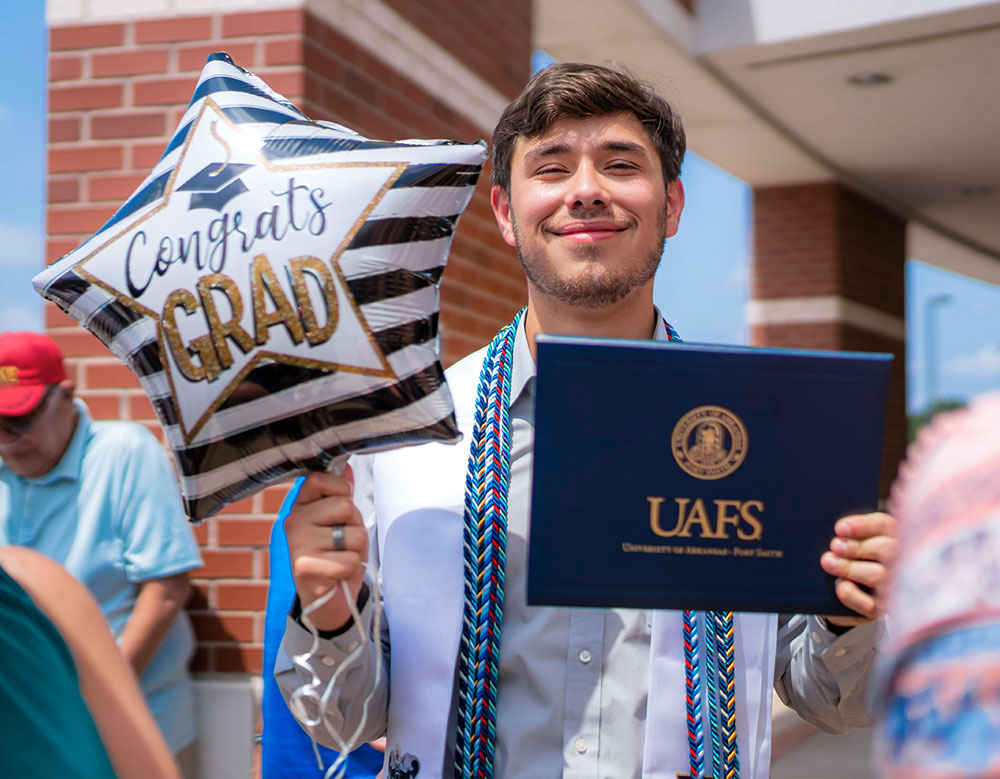 UAFS graduate smiles for the camera holding his diploma and a