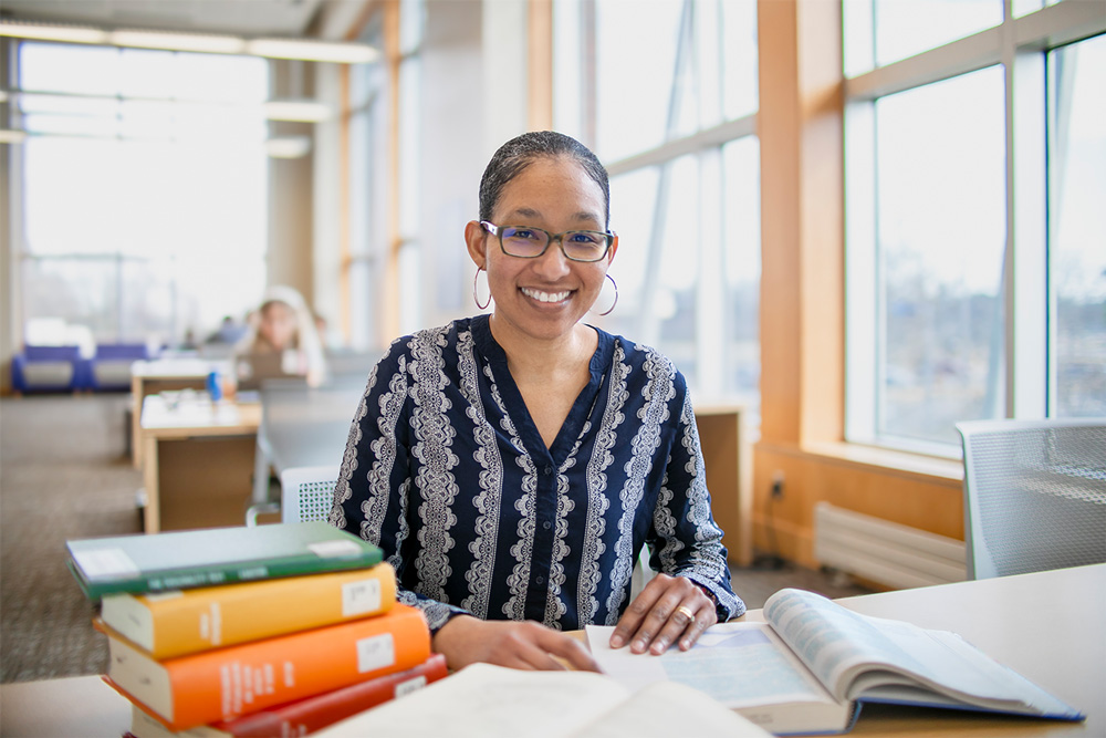 A UAFS psychology professor, Dr. Nicha Otero, browses a stack of books she has in front of her while sitting at a table on the second floor of the Boreham Library.