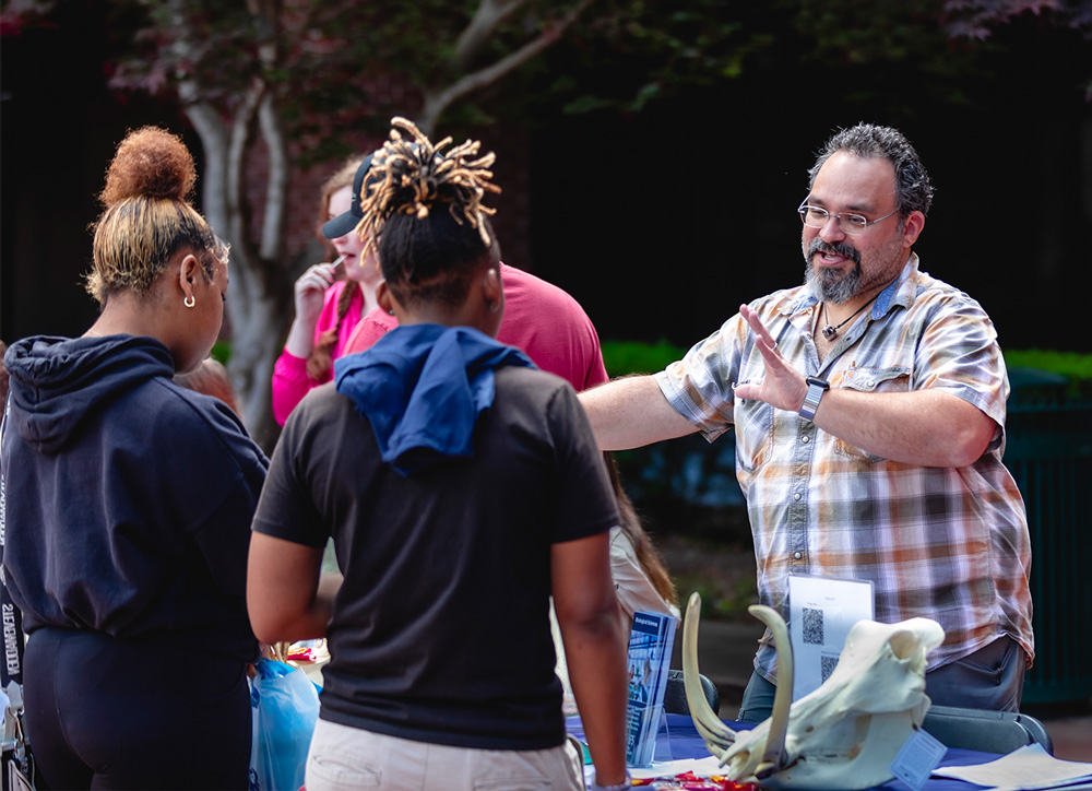 Dr. Jason Ortega, right, talks to students about the UAFS College of Arts and Sciences with a skull of a warthog on the table.