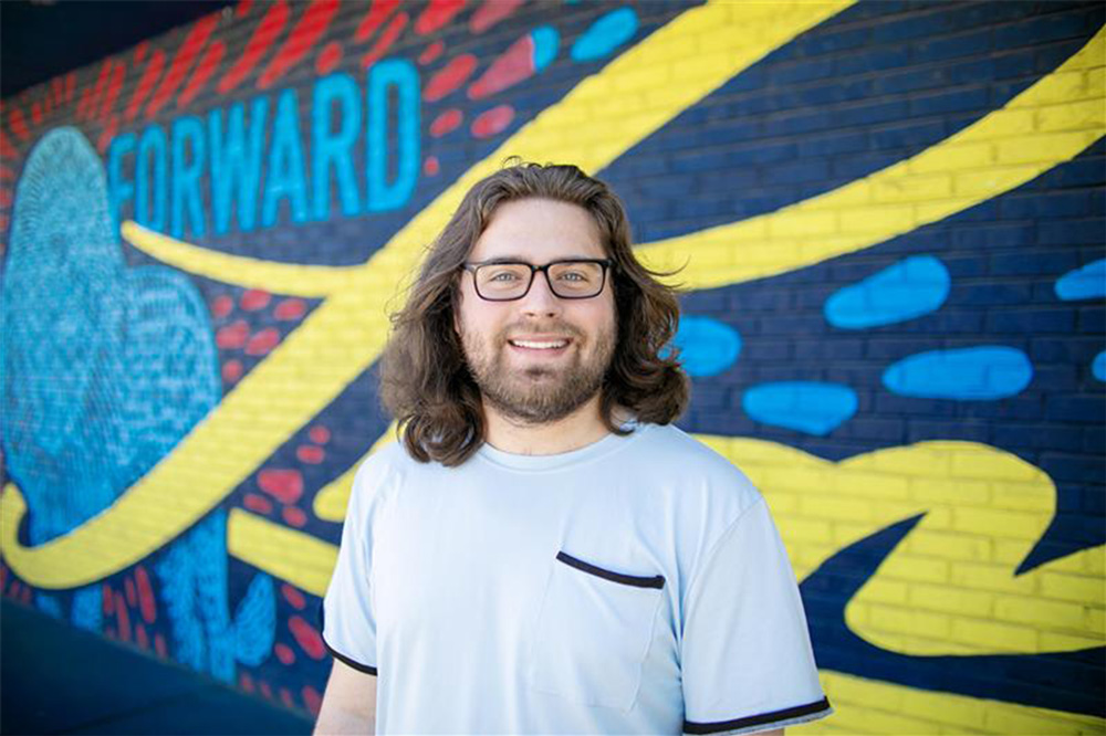 Troy Rodriguez smiles in front of the lion mural at the UAFS Alumni Center